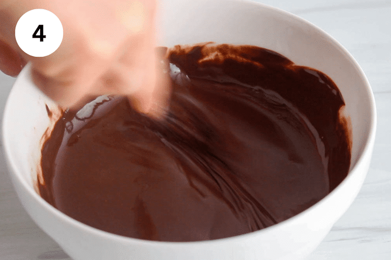 A small whisk stirring in a bowl with melted chocolate.