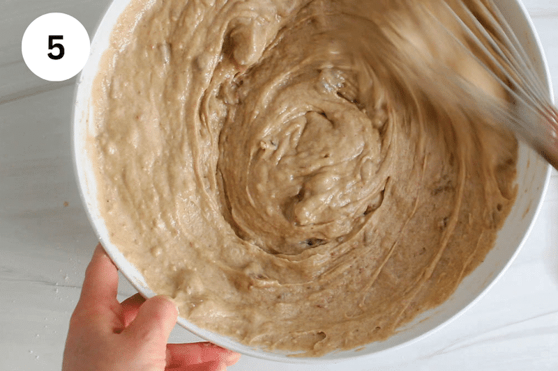 A large whisk stirring in a large bowl filled with a cake batter.