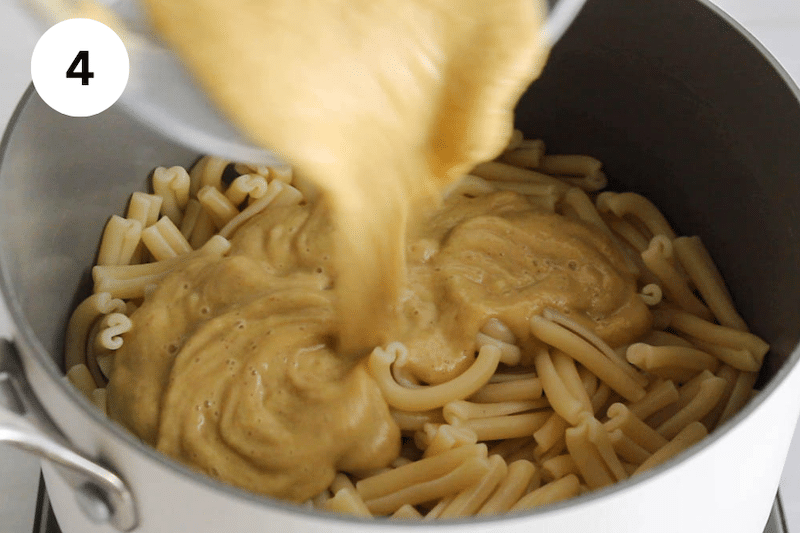 Blended pasta sauce pouring in a large pot with cooked pasta.
