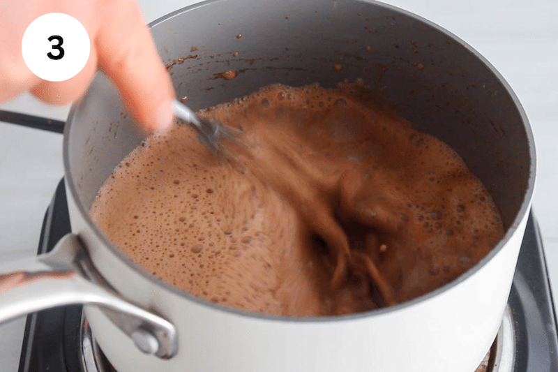 A whisk stirring in a small saucepan with a hot chocolate mix.
