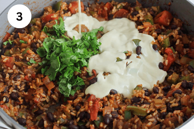 A pan with a saucy rice and bean mixture topped with cilantro and cheese sauce.