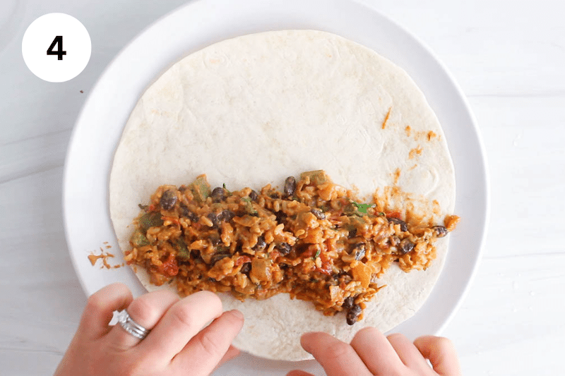 A tortilla with a bean and rice mix over with hands rolling it.