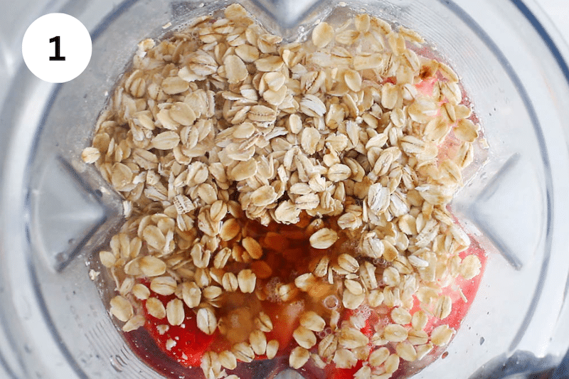 View inside a blender filled with strawberries, oats and water.