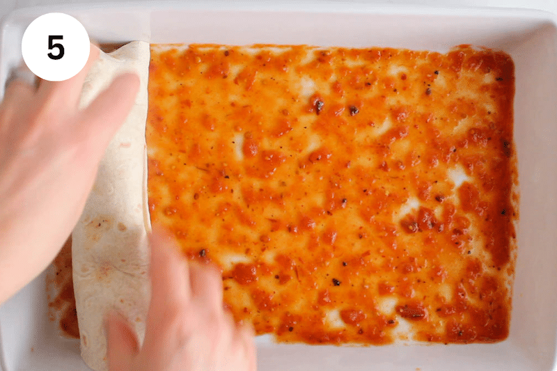 A large baking dish with red enchilada sauce at the bottom.