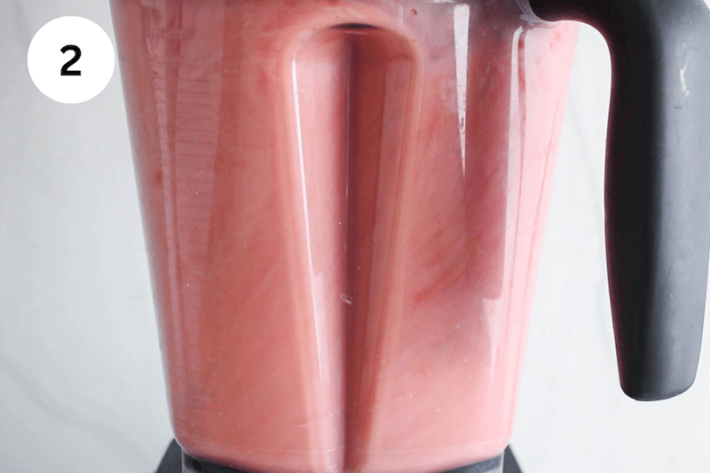 A bright pink mix blending in a blender.