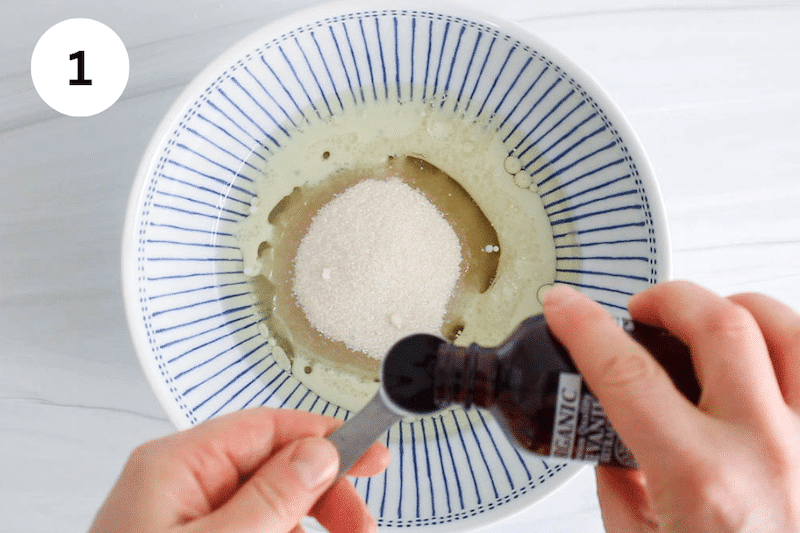 A bowl with oil and sugar and vanilla extract pouring in a teaspoon over the bowl.
