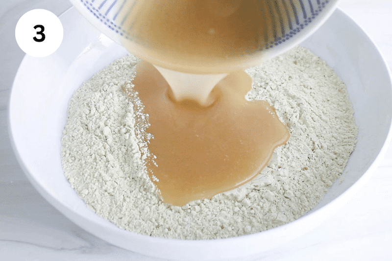 A creamy mixture pouring in a bowl with flour.