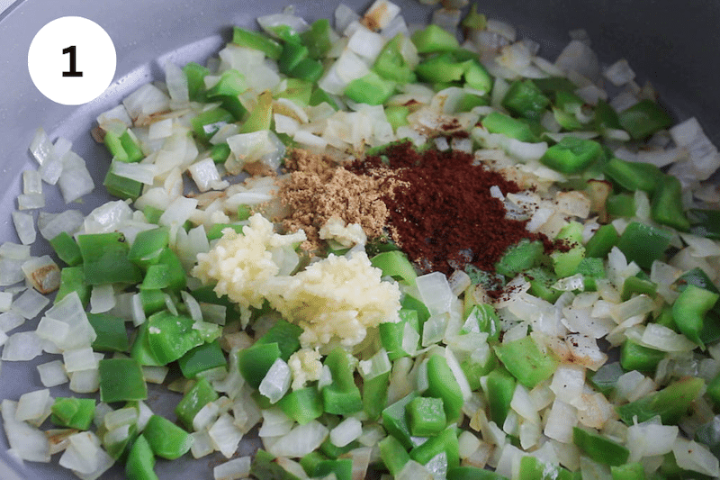 A large pan cooking onion, green bell pepper, garlic and spices.