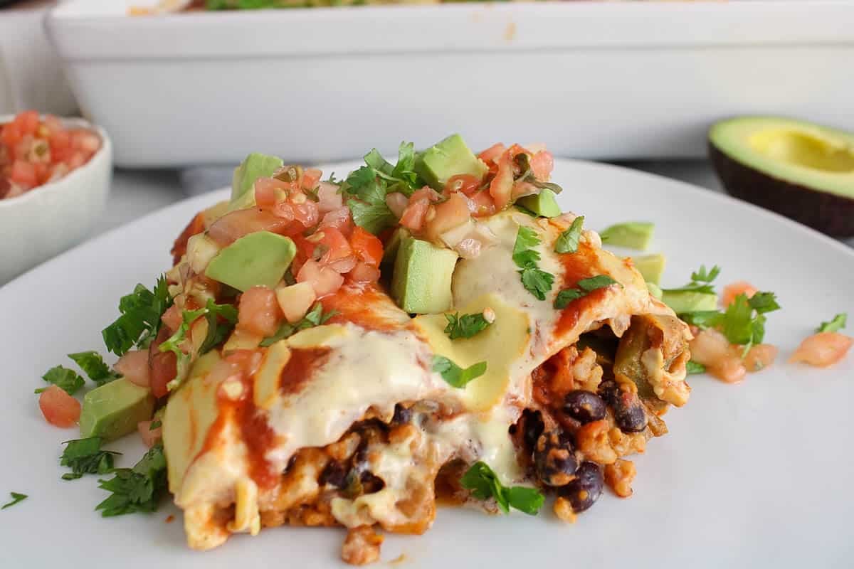 Sliced dairy-free bean and rice enchiladas on a plate topped with avocado.