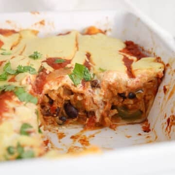 Sliced bean and rice enchiladas in a baking dish with a creamy cheesy sauce coming out.