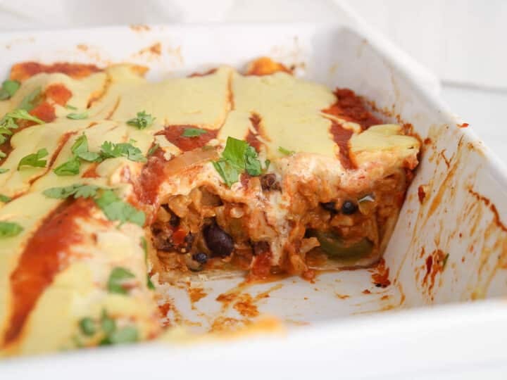 Sliced bean and rice enchiladas in a baking dish with a creamy cheesy sauce coming out.