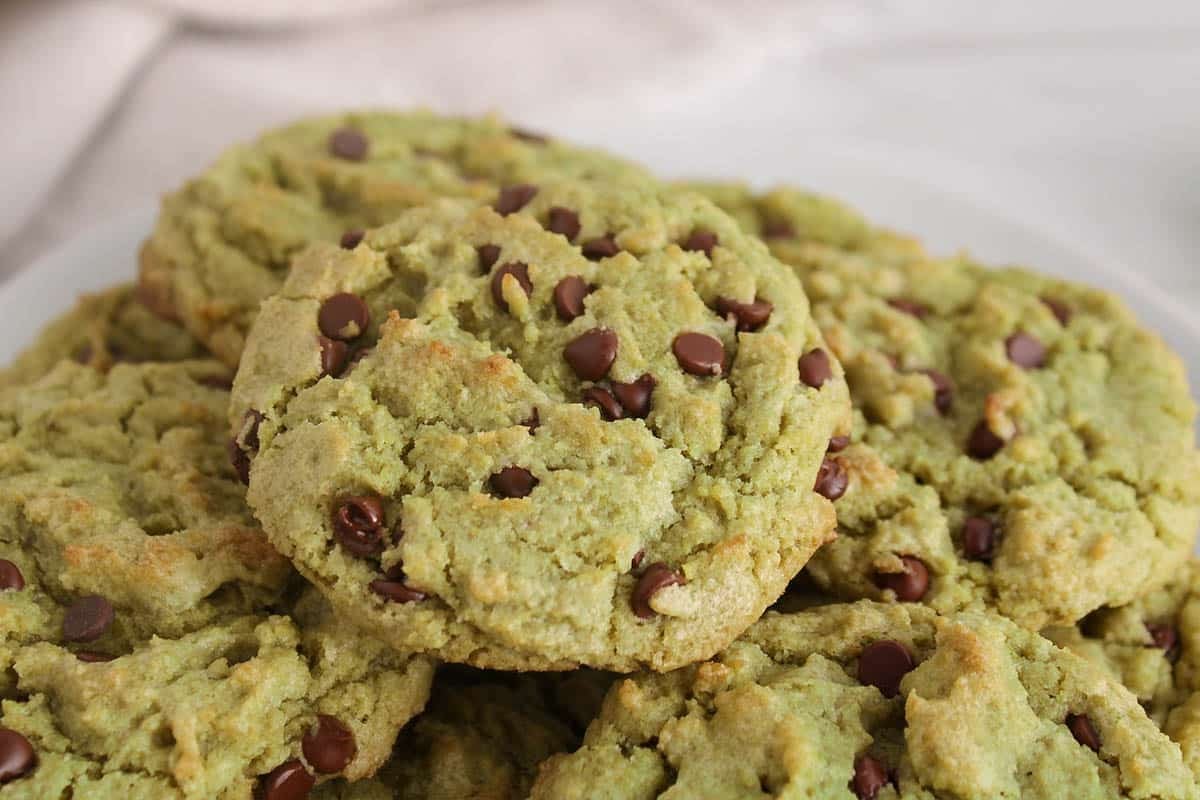 Vegan matcha cookies with chocolate chips piled on a plate.