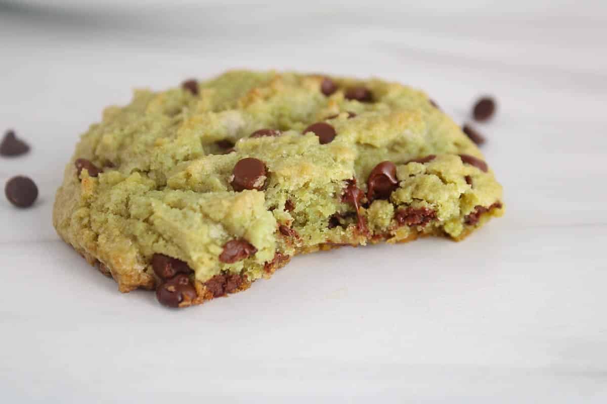 A vegan matcha chocolate chip cookie with a bite taken off on a white table.