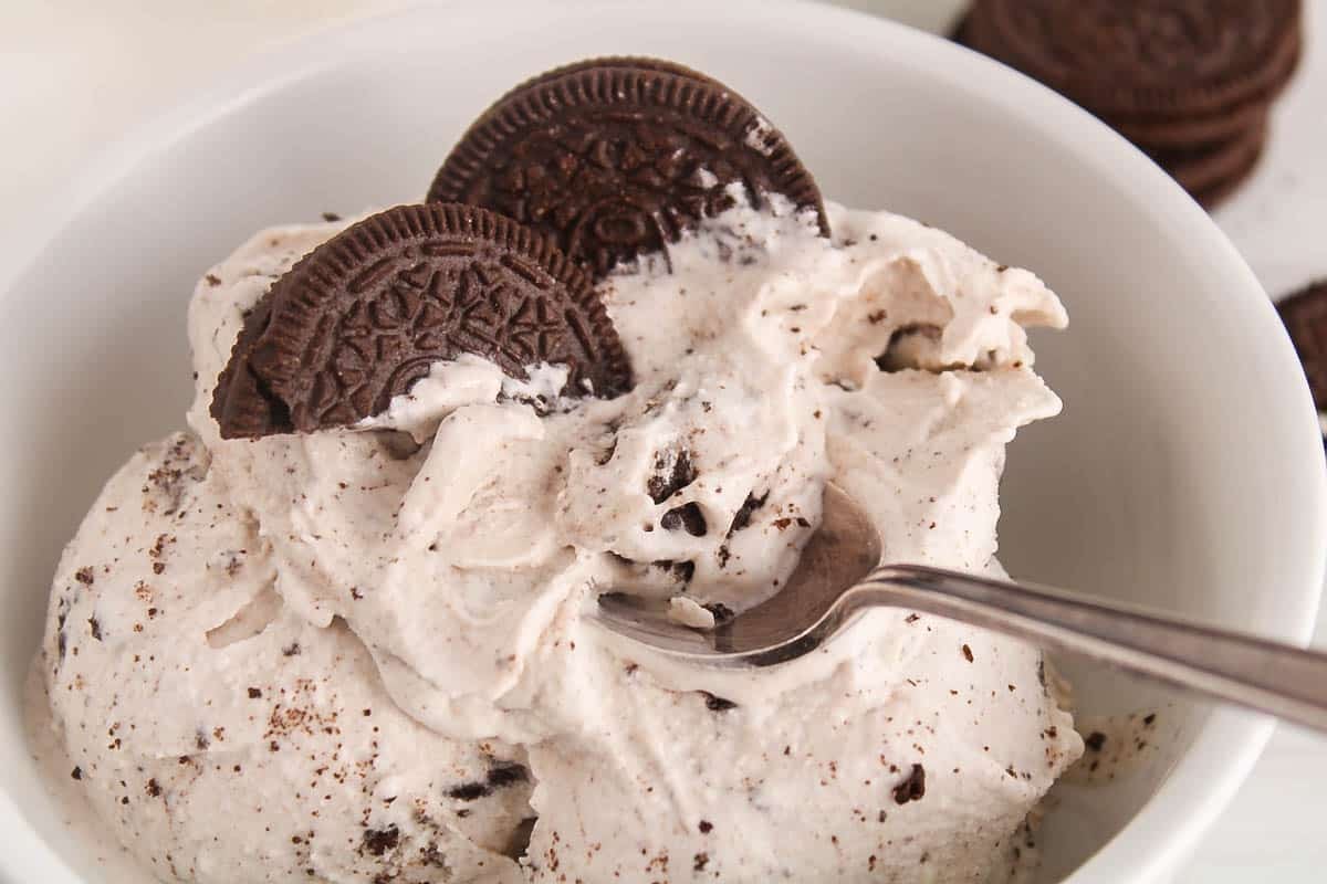A spoon taking a spoonful of dairy-free cookie and cream ice cream from a bowl.