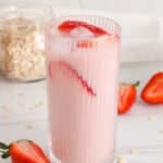 Tall see-through glass of pink dairy-free strawberry oat milk.