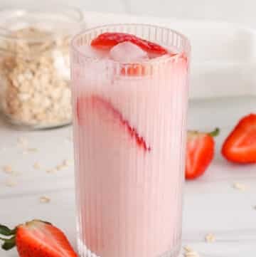 Tall see-through glass of pink dairy-free strawberry oat milk.