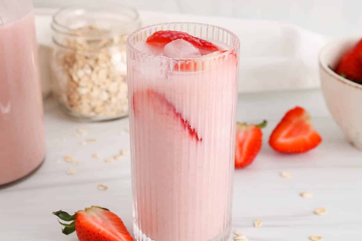 Tall see-through glass of pink dairy-free strawberry oat milk.