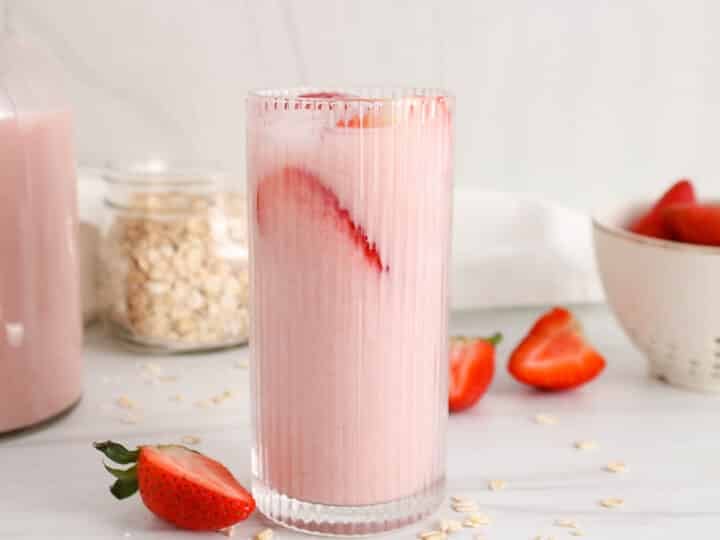 Glass of strawberry oat milk with ice cubes and sliced fresh strawberries.