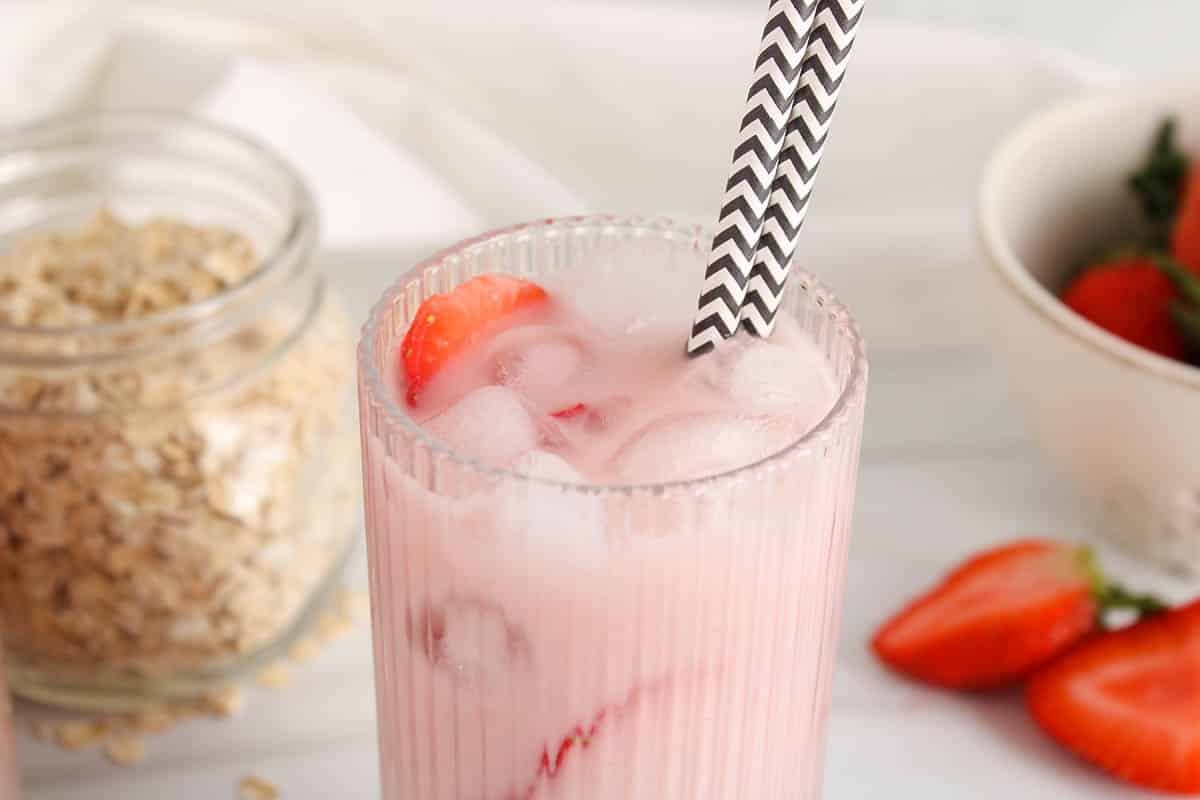 Top part of a glass of dairy-free strawberry oat milk with black and white straws.
