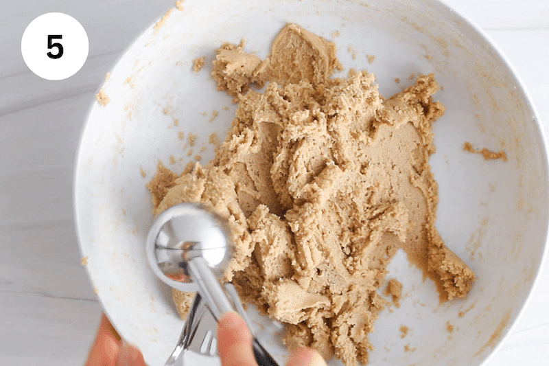 An ice cream scoop taking some cookie dough from a large bowl.