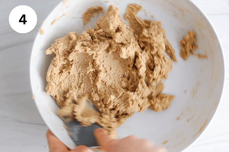 A spatula mixing a cookie dough in a large white bowl.