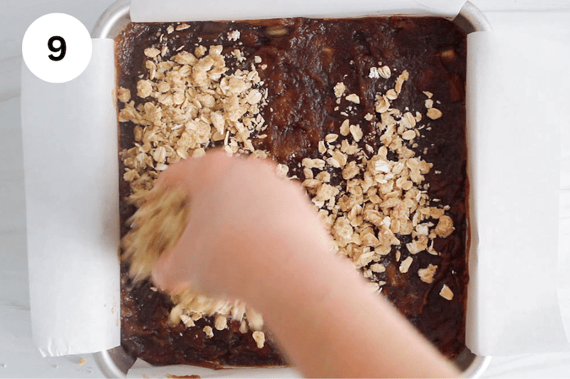 A hand adding a oat mix over a layer of mashed dates in bars.
