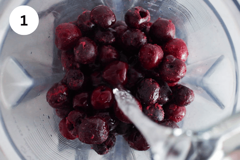Water pouring in a blender filled with frozen cherries.