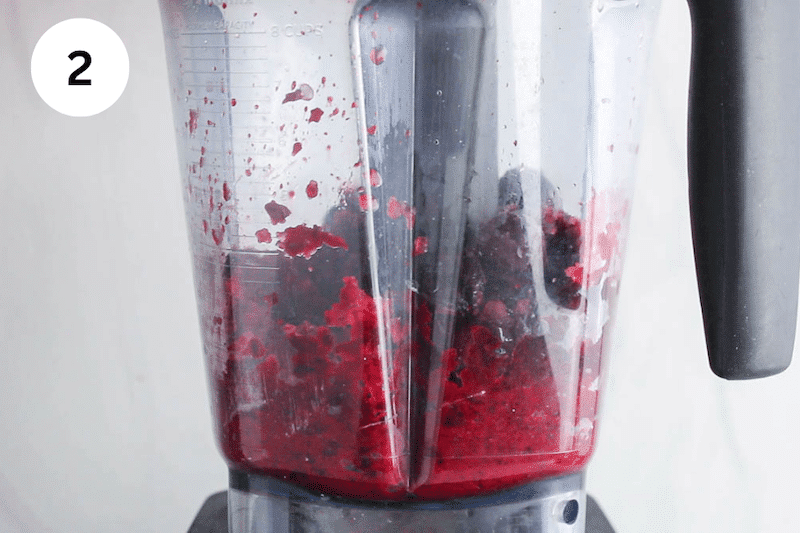 A blender blending some frozen cherries with water.