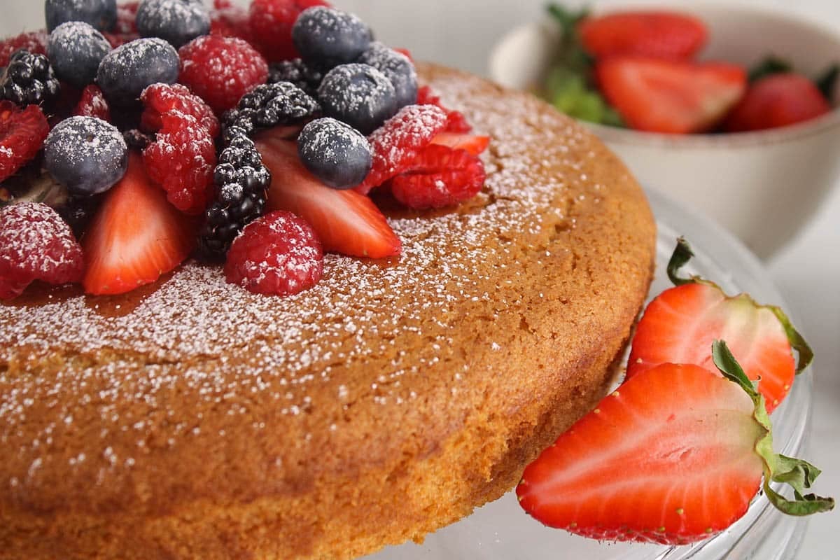 Showing the side of a vegan olive oil cake topped with berries and powdered sugar.