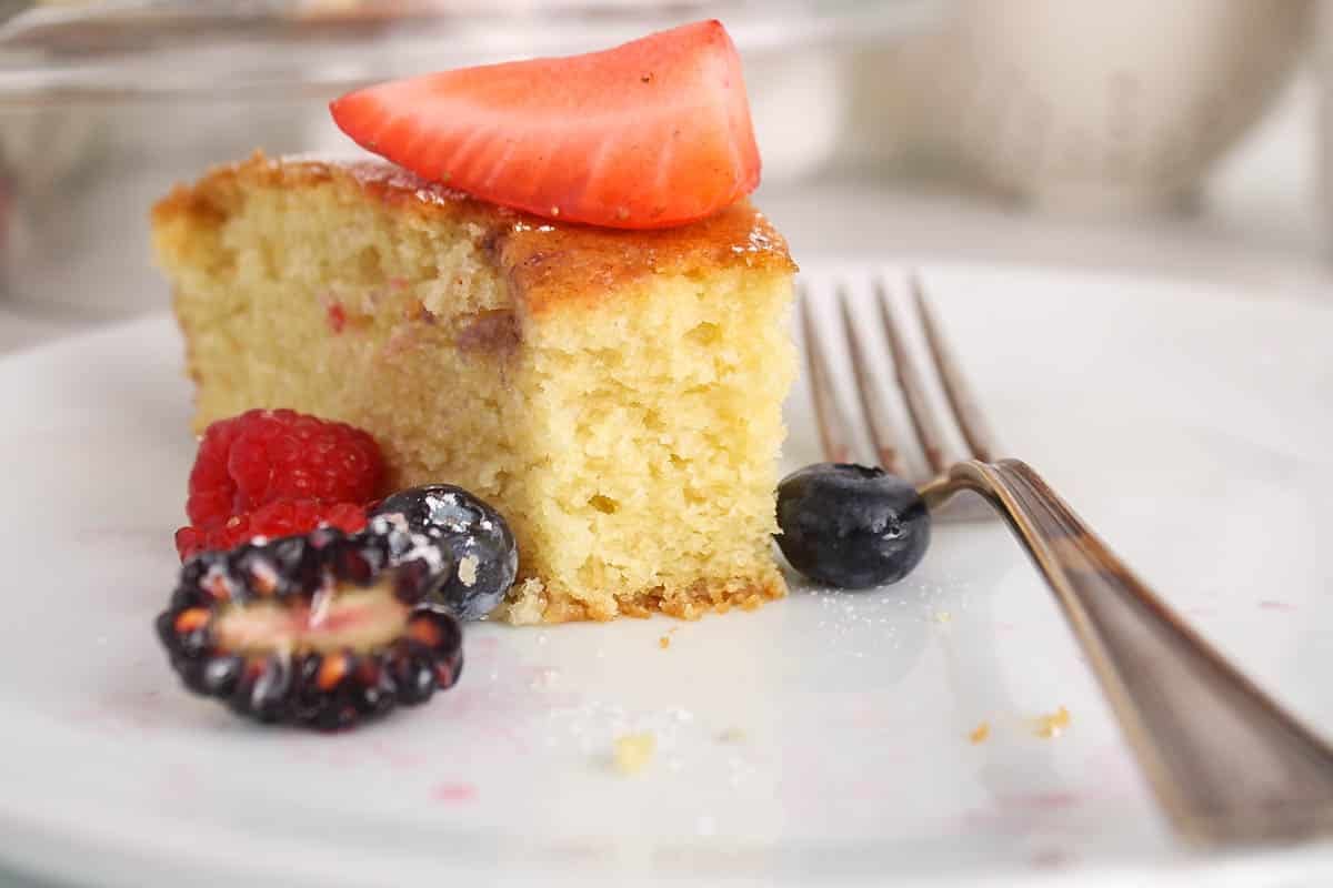 A slice of vegan olive oil cake on a plate with berries.