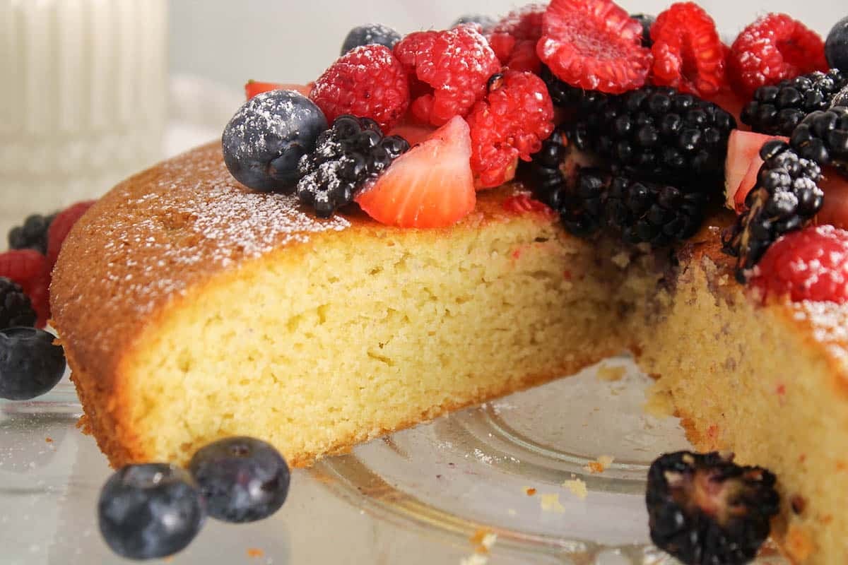 A half sliced round olive oil cake on a glass cake stand.