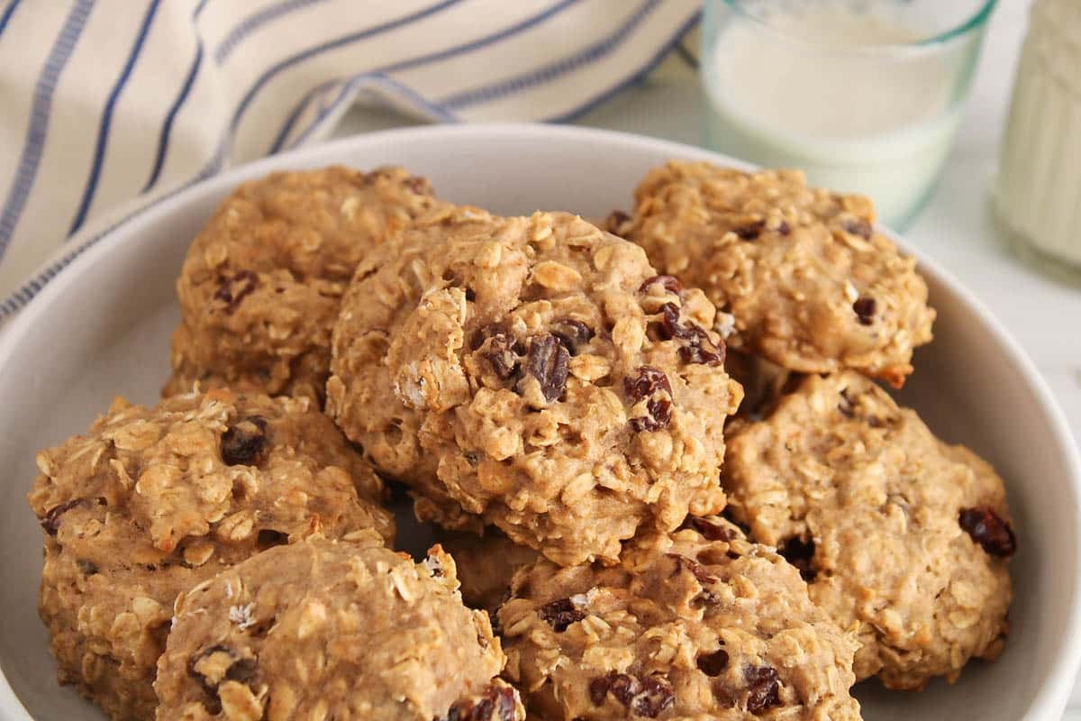 Vegan oat and raisin protein cookies on a plate with a glass of milk beside.