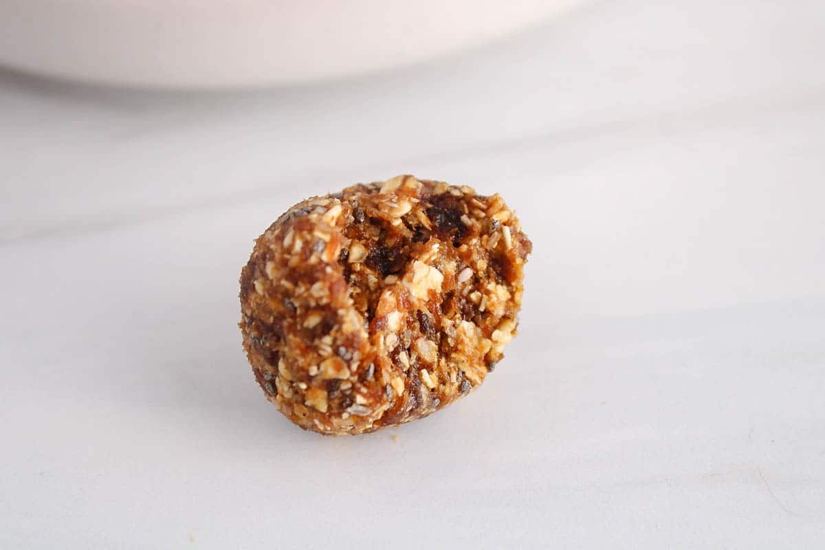 A healthy apricot bliss ball with a bite taken off on a white table.