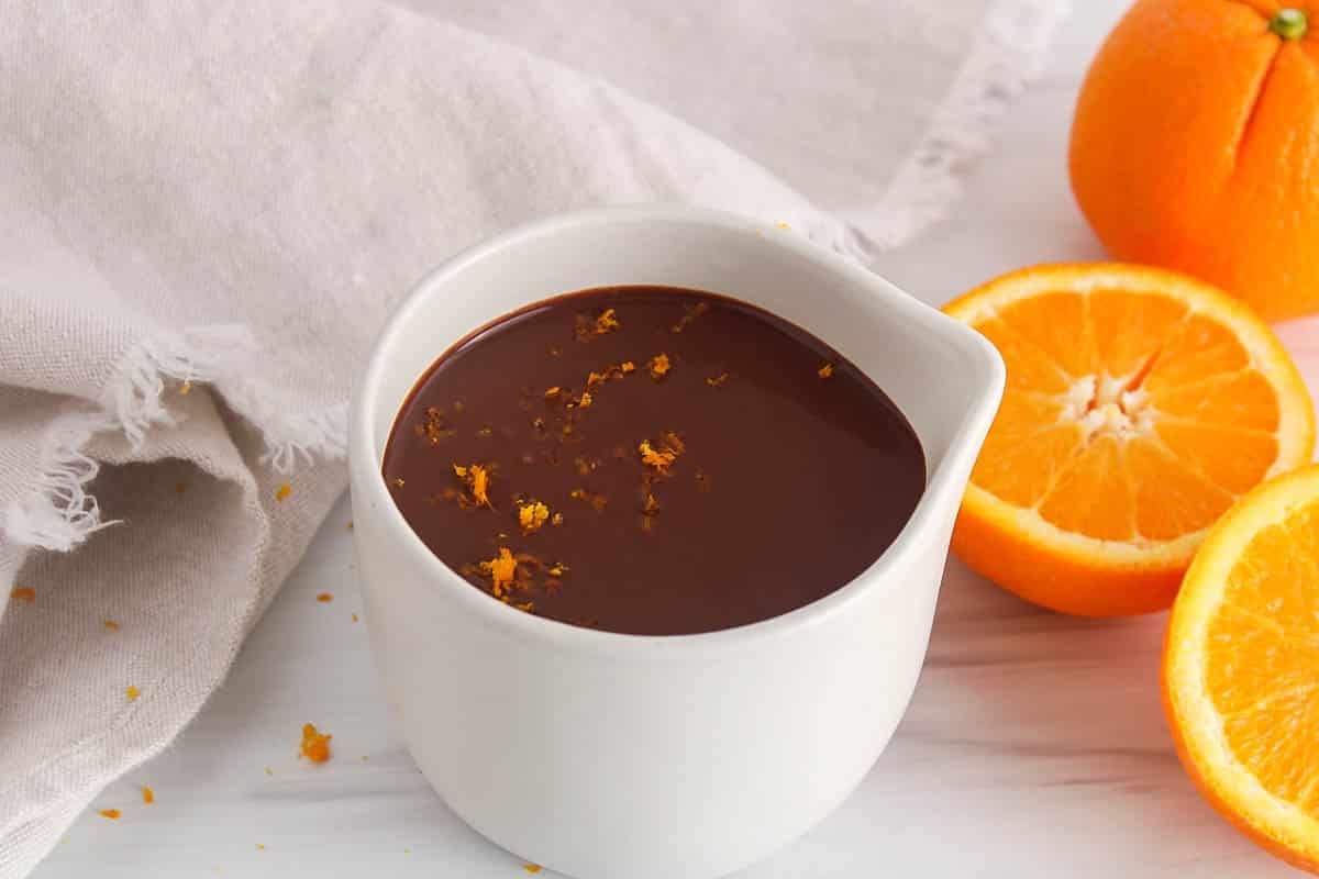 White jar filled with a vegan orange chocolate ganache garnished with orange zest.