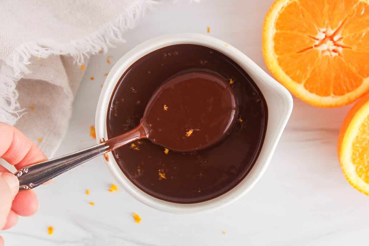 A large spoon taking some orange chocolate ganache from a white jar.