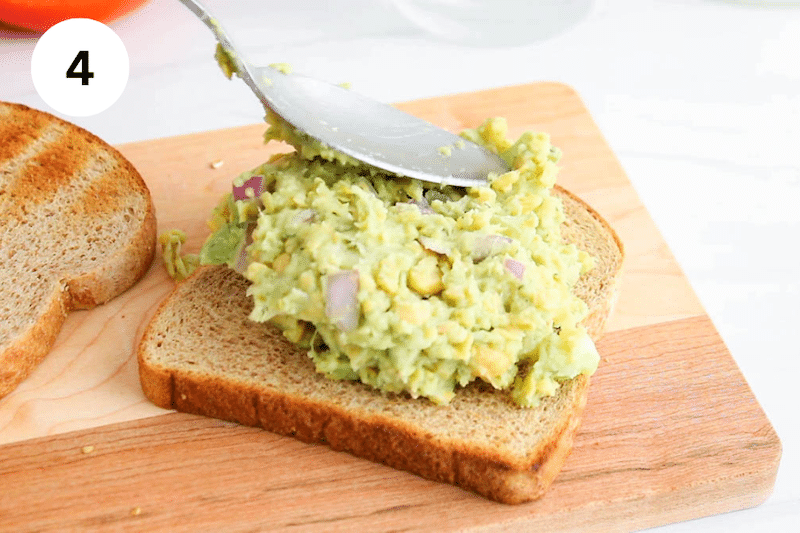 A large spoon adding avocado chickpea mixture over toasted bread.