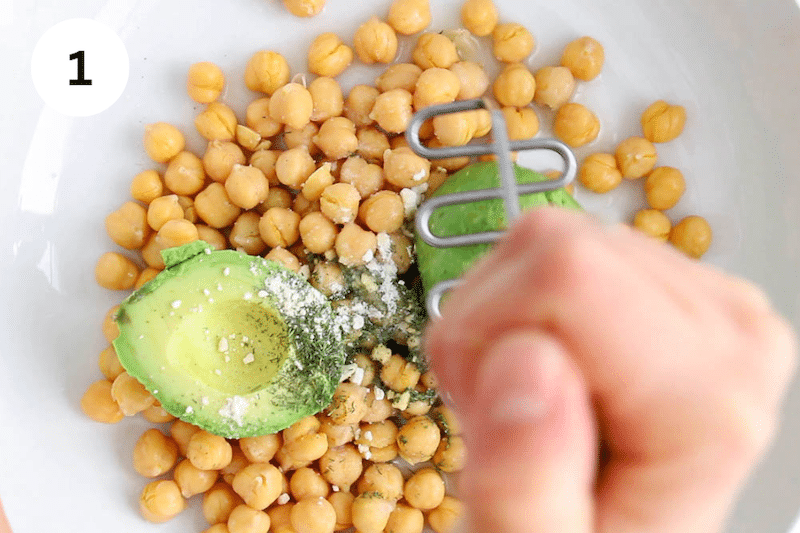 A potato masher mashing chickpeas with avocado.