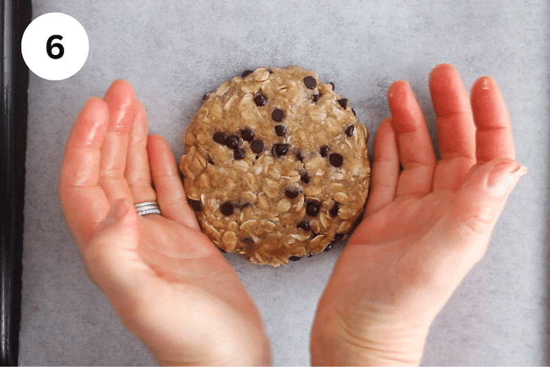 Hands shaping cookie dough into a large cookie.