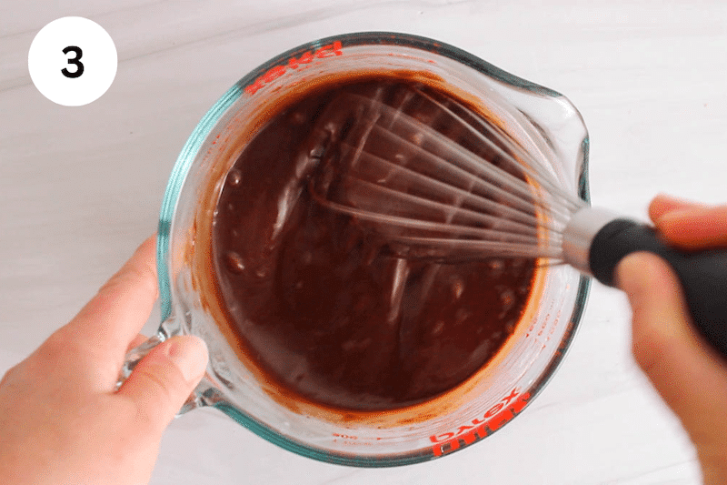 A whisk stirring a chocolate sauce.