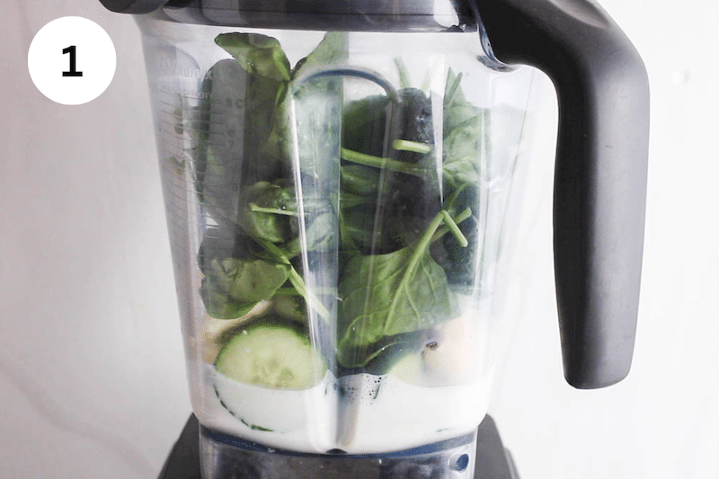 Blender filled with oat milk, cucumber, frozen fruit and spinach.