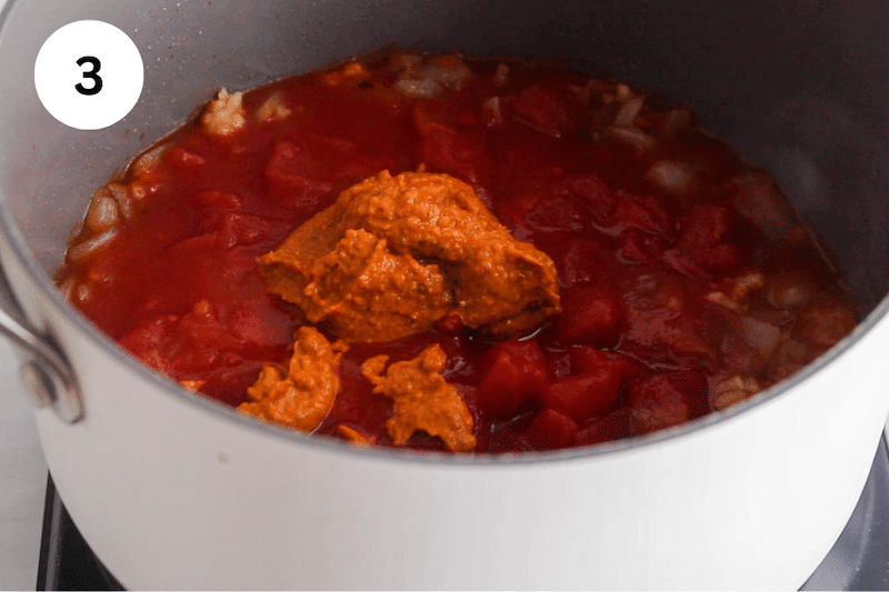 A small pot with tomatoes and red pesto sauce over.