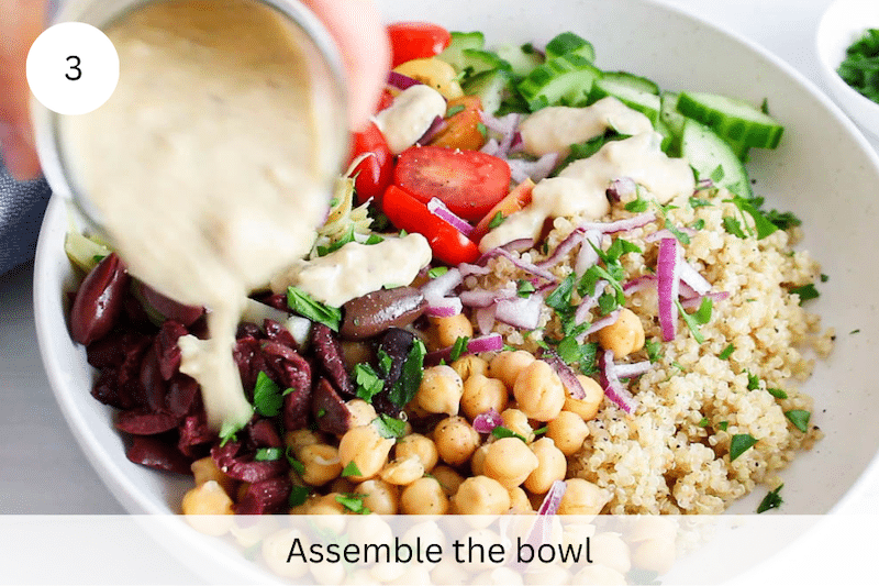A jar of hummus sauce pouring over a Mediterranean quinoa bowl.