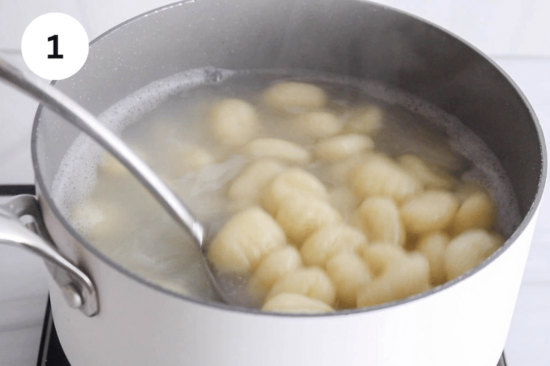 A large spoon taking some boiling gnocchi from a large pot of boiling water.
