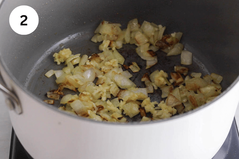 A small pot cooking some onion and garlic.