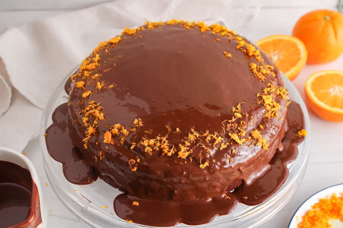 Vegan Chocolate Orange Ganache Cake on a glass cake platter covered with orange zest.