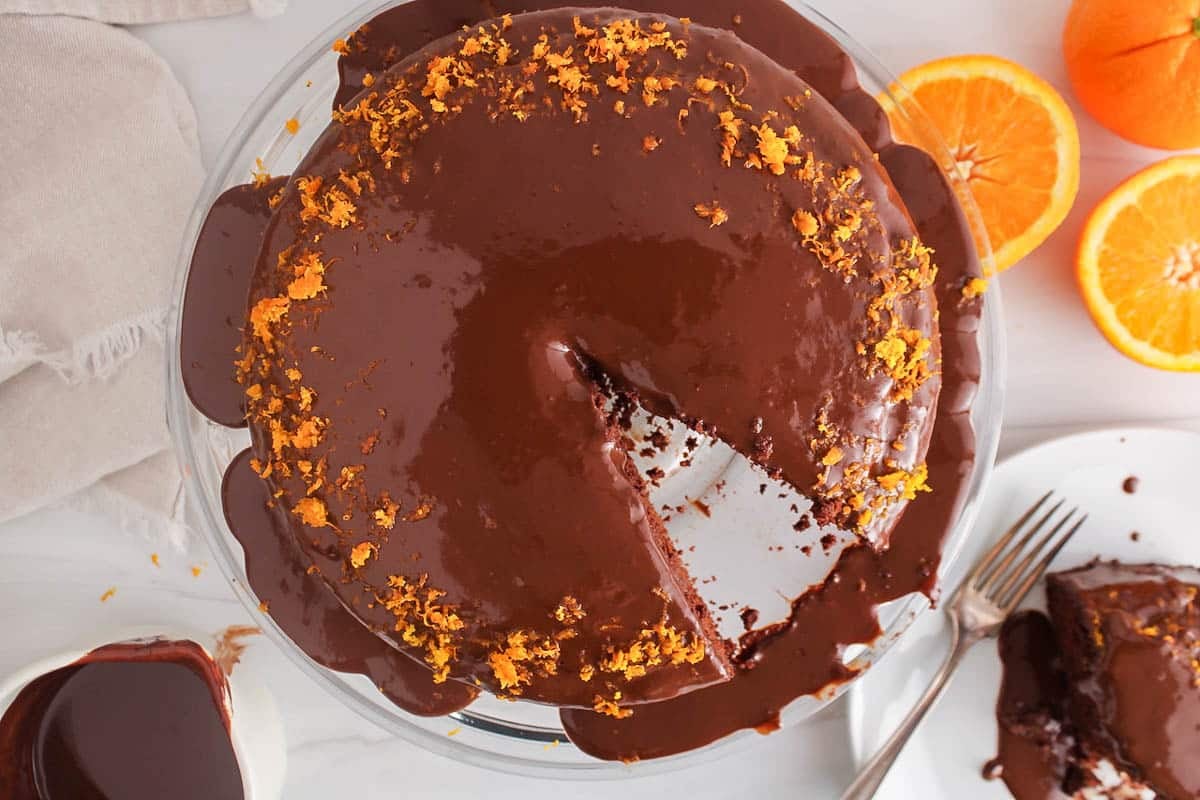 Slice of Vegan Chocolate Orange Ganache Cake on a plate with a slice taken off.