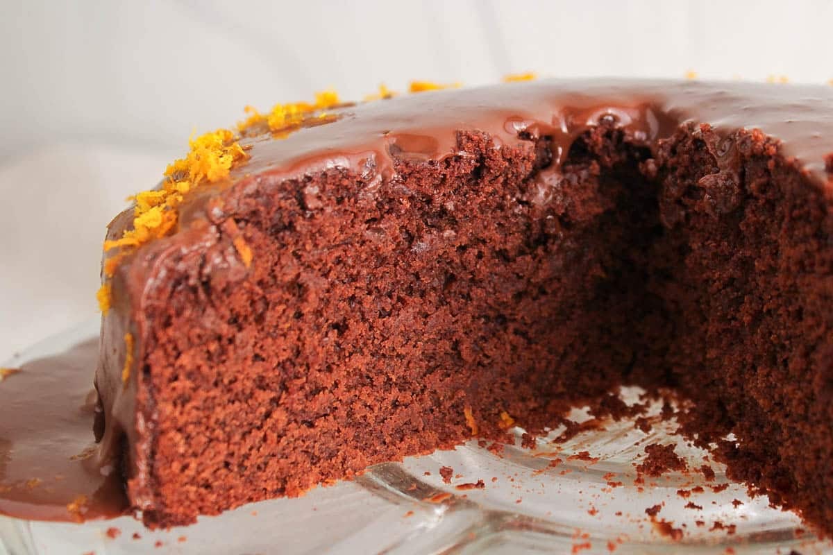 Slice of Vegan Chocolate Orange Ganache Cake on a plate with a slice taken off.