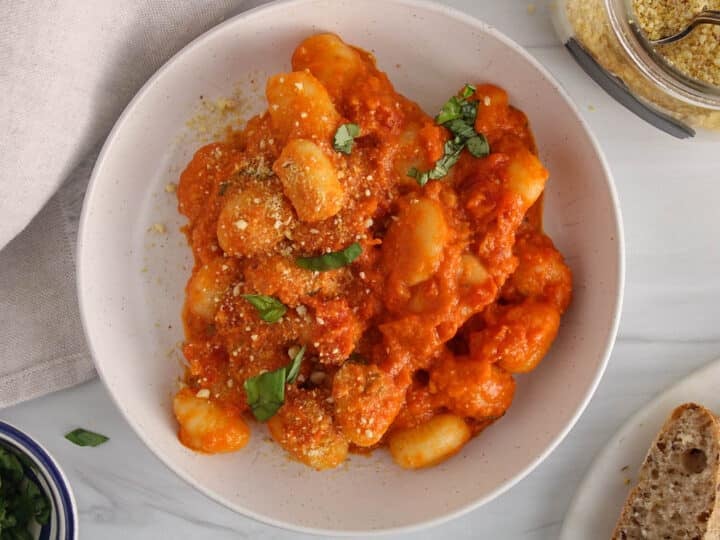 Red pesto gnocchi garnished with basil on a plate.