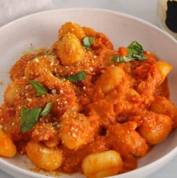 Saucy tomato and red pesto gnocchi garnished with basil on a plate.