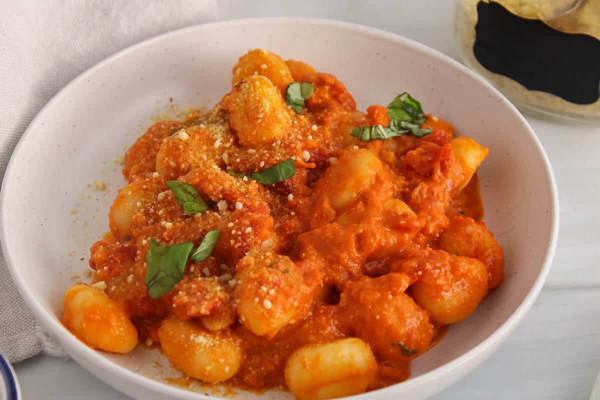 Saucy tomato and red pesto gnocchi garnished with basil on a plate.